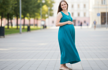Kobieta w ciąży w stylowej codziennej stylizacji stoi na mieście, uśmiechnięta i pewna siebie.